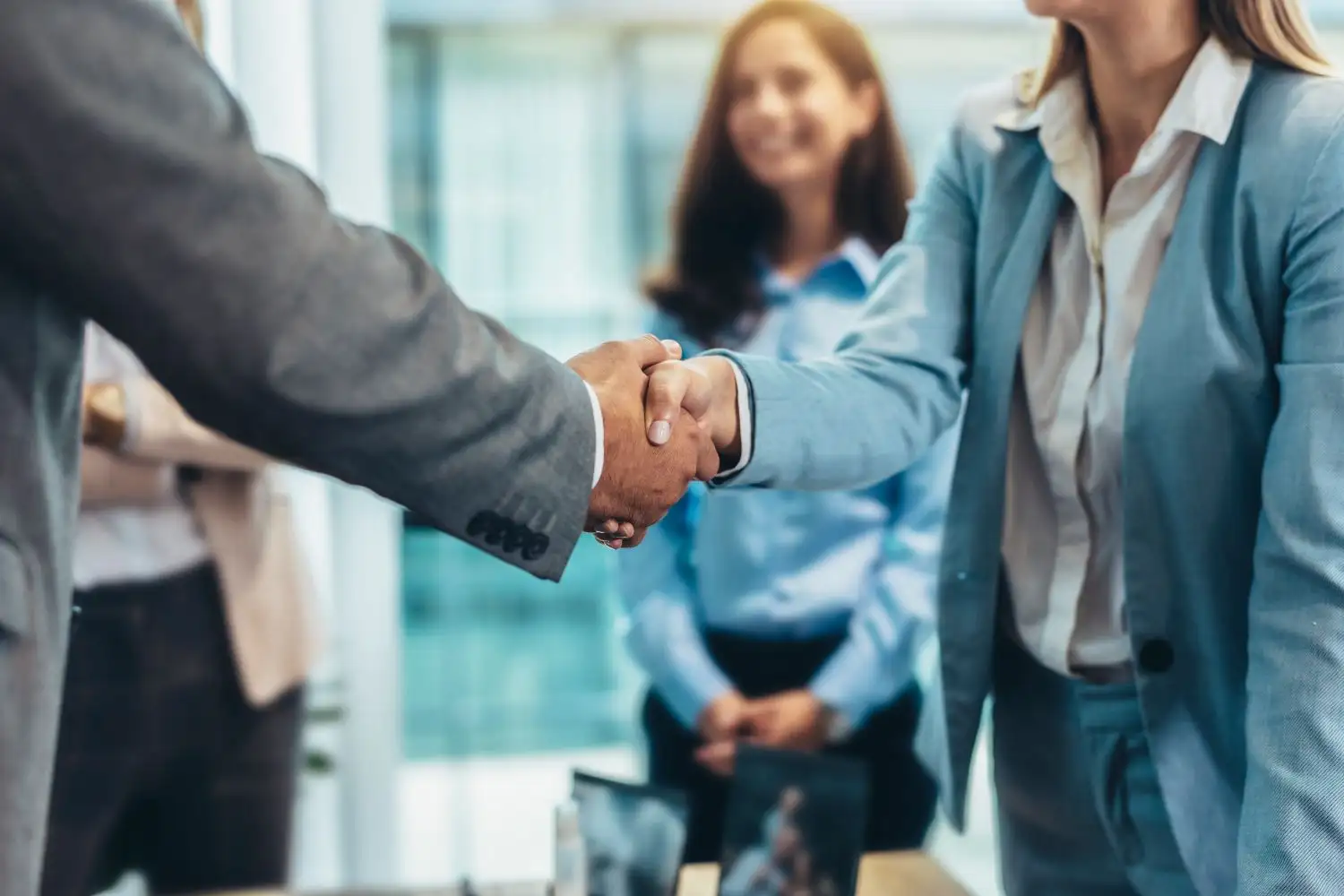 Two people shaking hands with people around smiling
