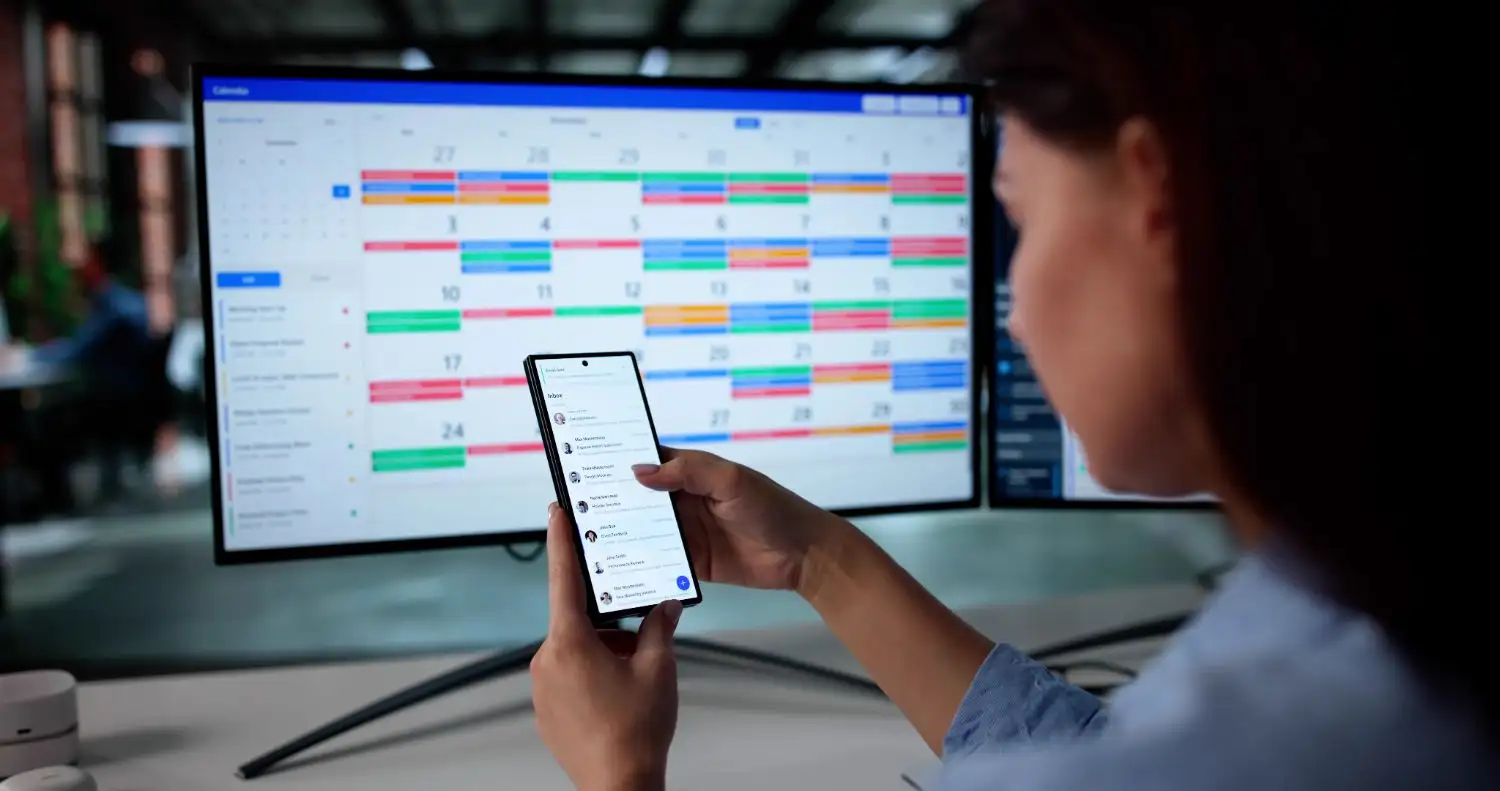 Woman looking on her phone with computer in background